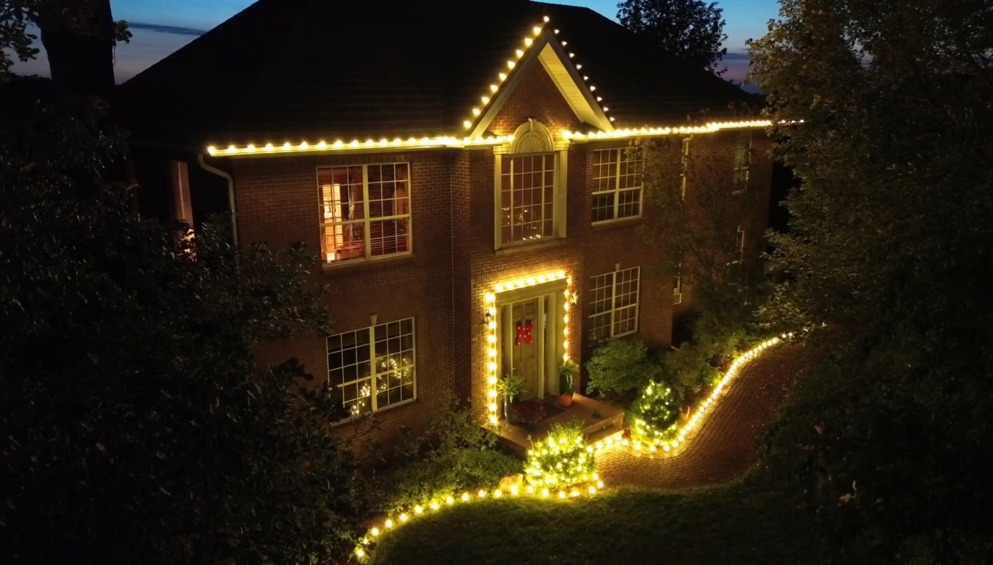 Two story brick home lit by Crown Lighting: roofline, front door, shrubs and walkway